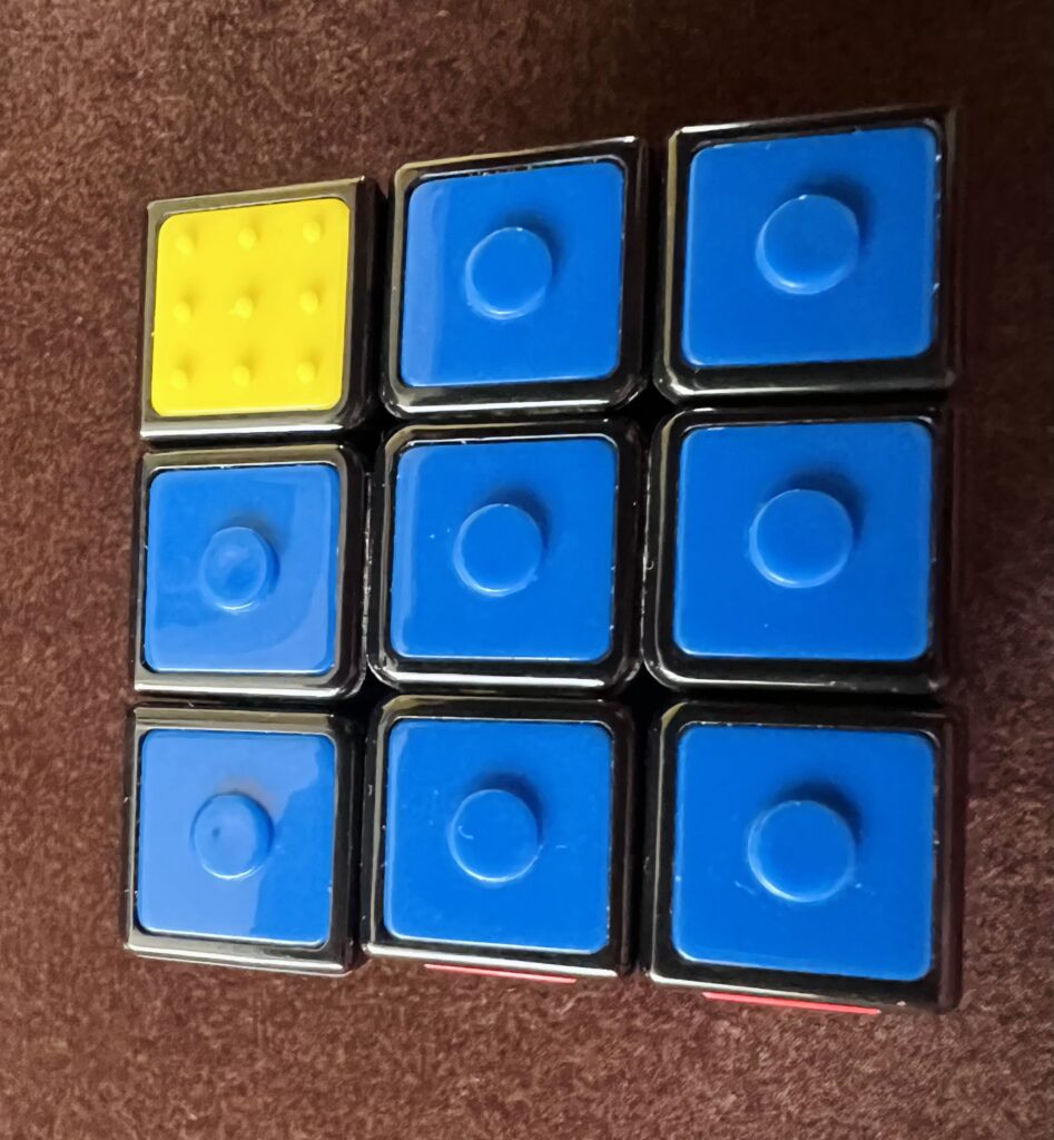 Czołowa ściana kostki Rubika, ułożona z niebieskich klocków. W lewym górnym rogu znajduje się żółte pole.