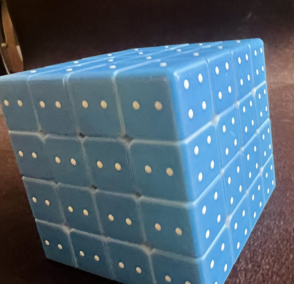 Ułożona niebieska kostka 4x4x4. Widoczne są w pełni ułożone ściany z oznaczeniami jednego, dwóch i czterech punktów.